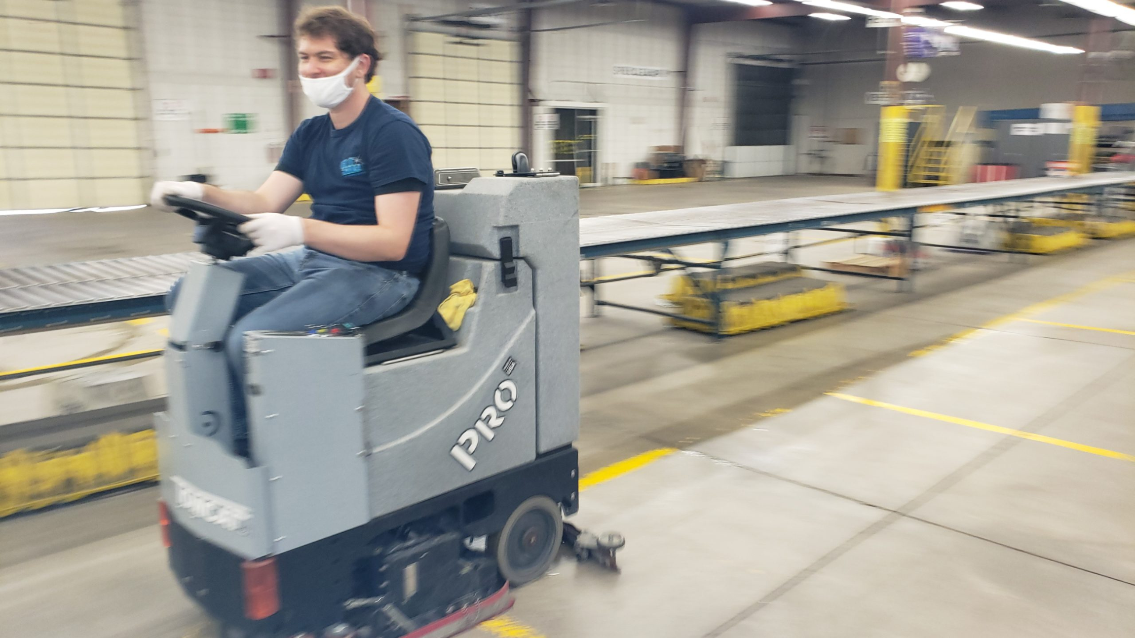 man riding industrial floor cleaner in industrial building