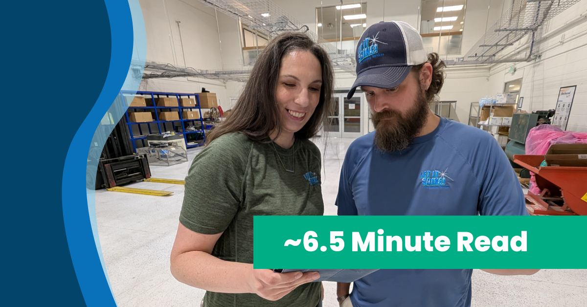 Two employees in branded shirts review a tablet together inside a warehouse with shelves and equipment in the background. Text overlay reads ‘~6.5 Minute Read.